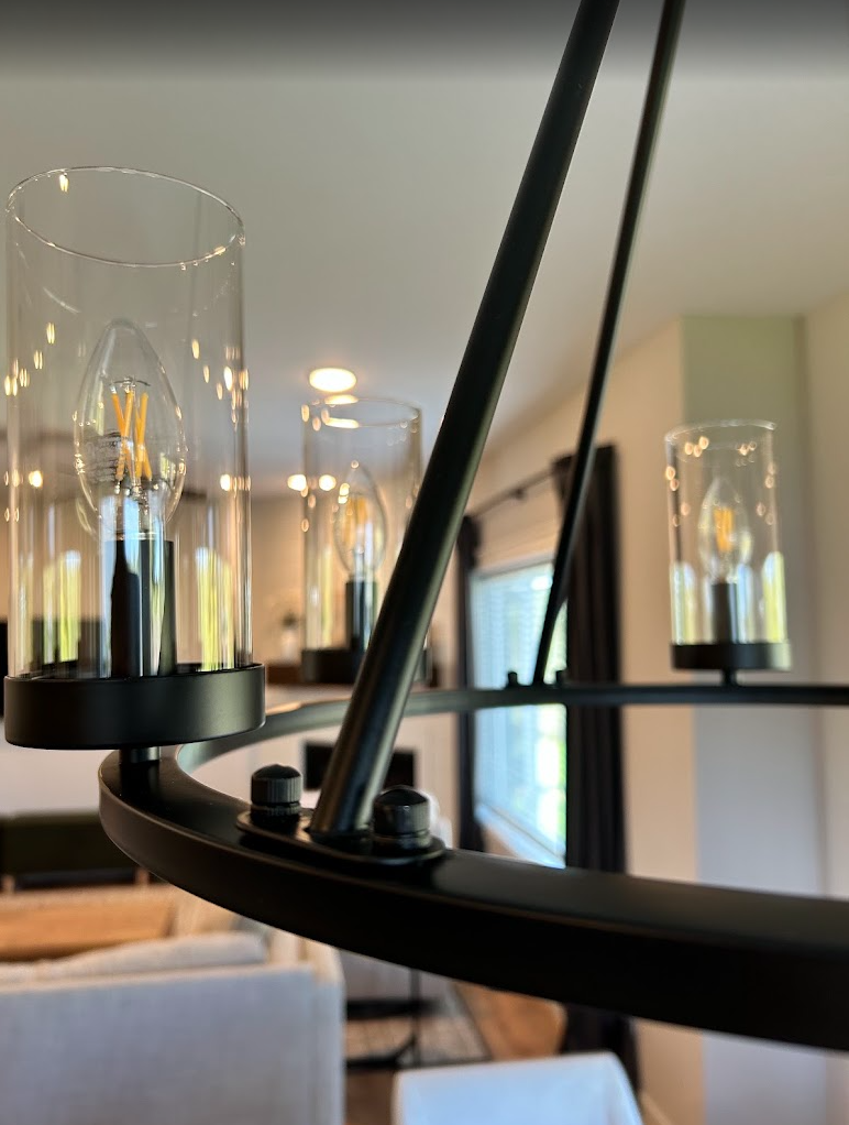A black iron chandelier with bulbs and clear glass shades, dusted clean
