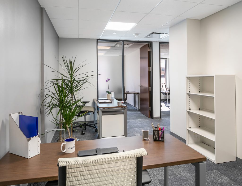 A bright, tidy small office with a wood desk and glass partition